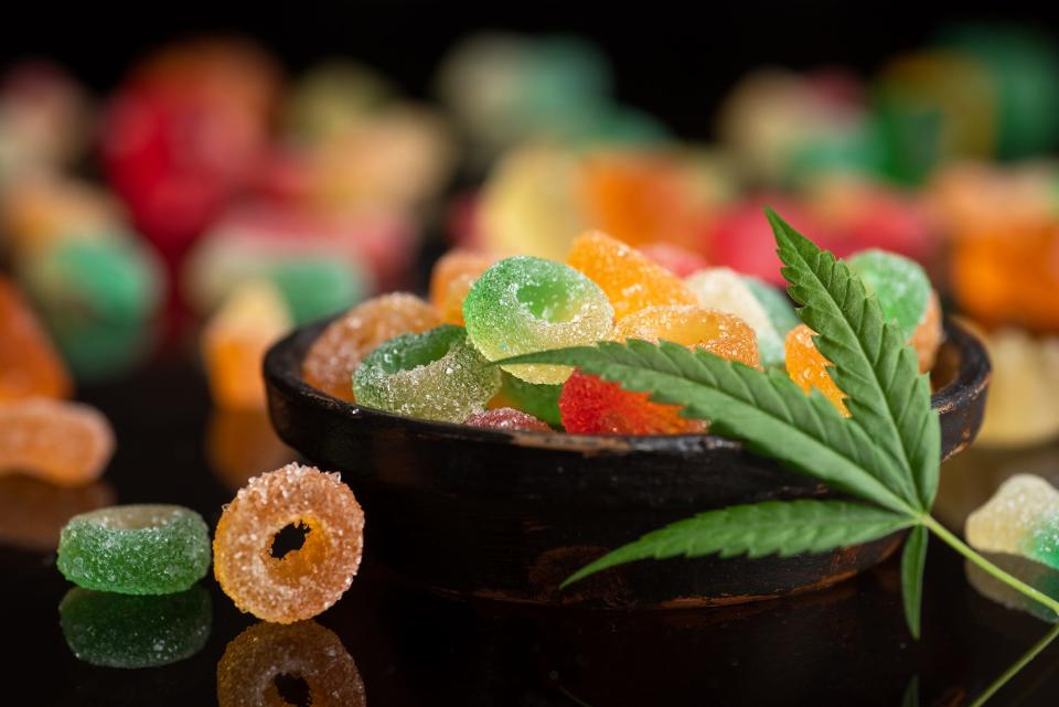 Colored gum candy jelly with marijuana leaves, on a black glass background. Sweet gummy candy with CBD, THC oil.
