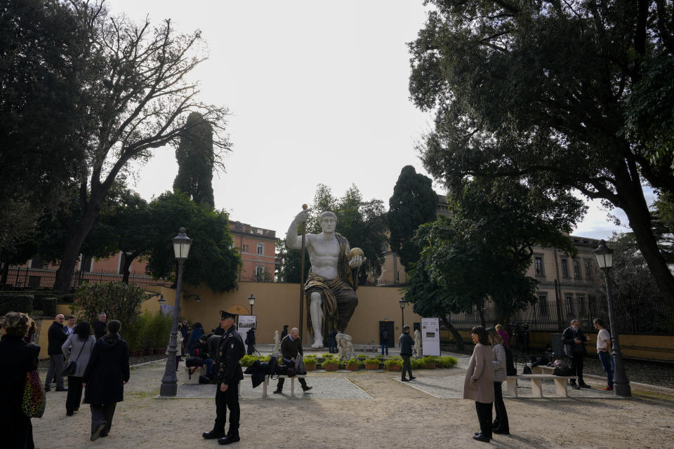 Visitors admire a massive, 13-meter (yard) replica of the statue Roman Emperor Constantine commissioned for himself after 312 AD that was built using 3D technology from scans of the nine giant original marble body parts that remain, as it was unveiled in Rome, Tuesday, Feb. 6, 2024. The imposing figure of a seated emperor, draped in a gilded tunic and holding a scepter and orb, gazing out over his Rome, is located in a side garden of the Capitoline Museums, just around the corner from the courtyard where the original fragments of Constantine's giant feet, hands and head are prime tourist attractions. (AP Photo/Andrew Medichini)