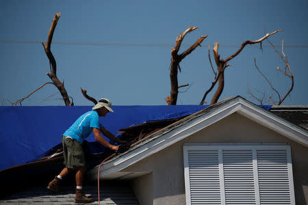 A roofer works on attaching a blue tarp to a roof following Hurricane Irma in Ramrod Key, Florida, U.S., September 18, 2017. REUTERS/Carlo Allegri