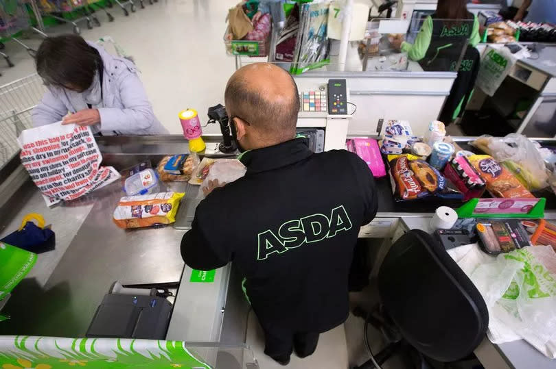 An employee scans a customer's purchases through the till at a check-out desk inside an Asda supermarket