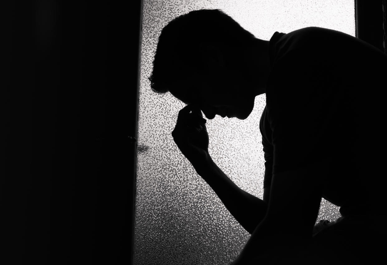 The silhouette of a young person, seemingly in distress, touching their hand to their forehead with their head down.
