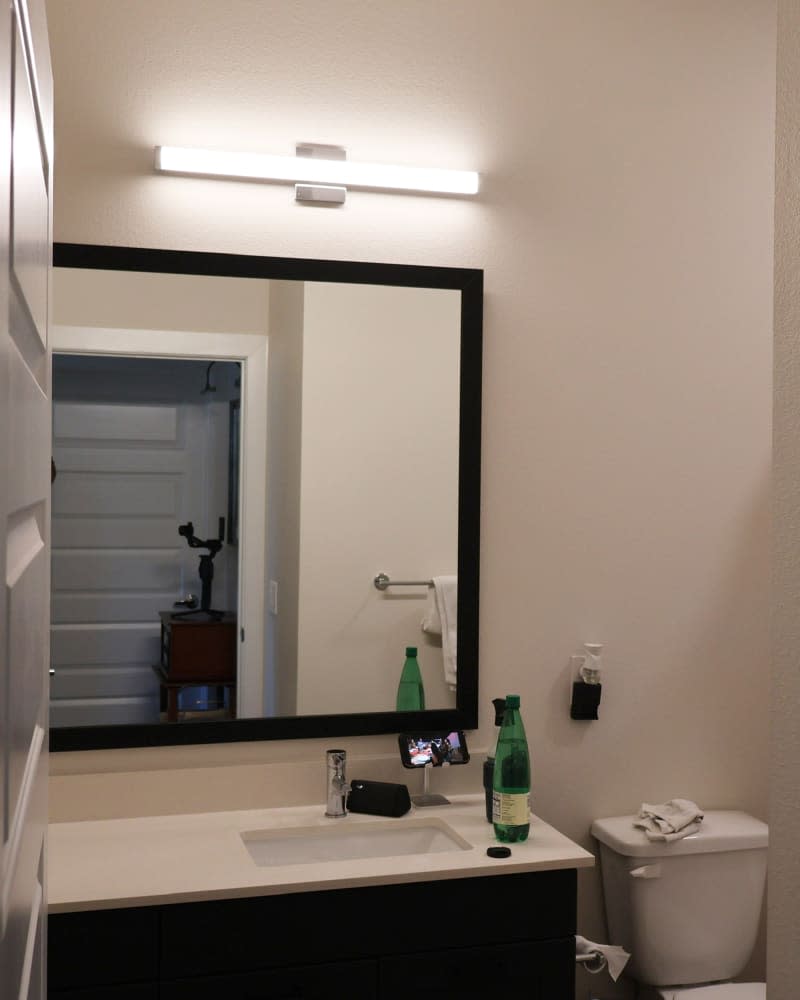 Beige bathroom with horizontal light over large, framed mirror.