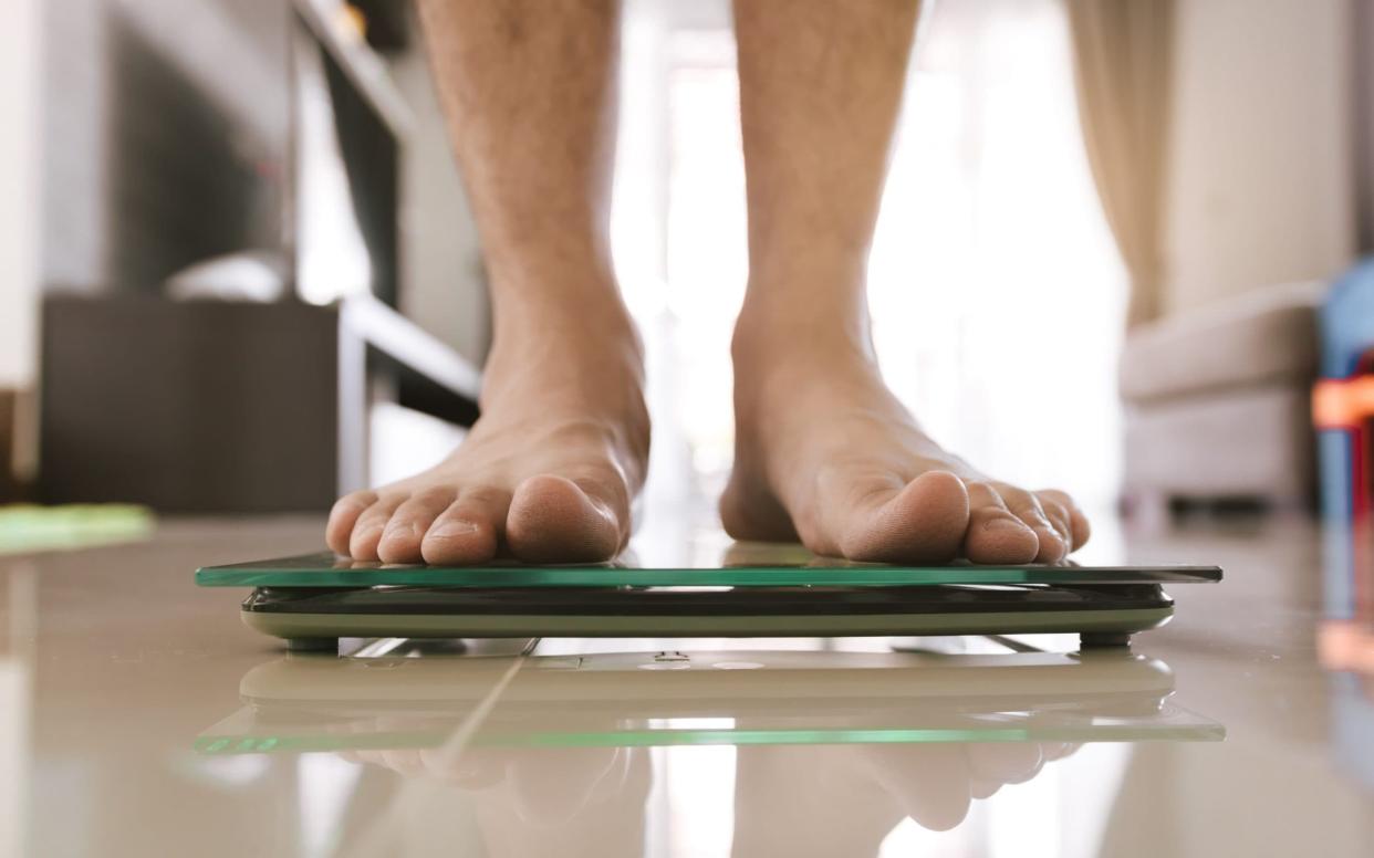 Close up of people feet standing on scale weighing - EyeEm/Getty Images