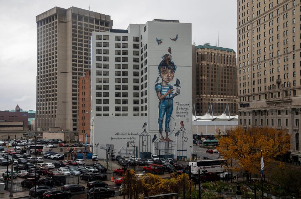 Dozens of cars are parked near a building in downtown Detroit with a giant mural of a girl singing surrounded by birds on Wednesday, Nov. 8, 2023.