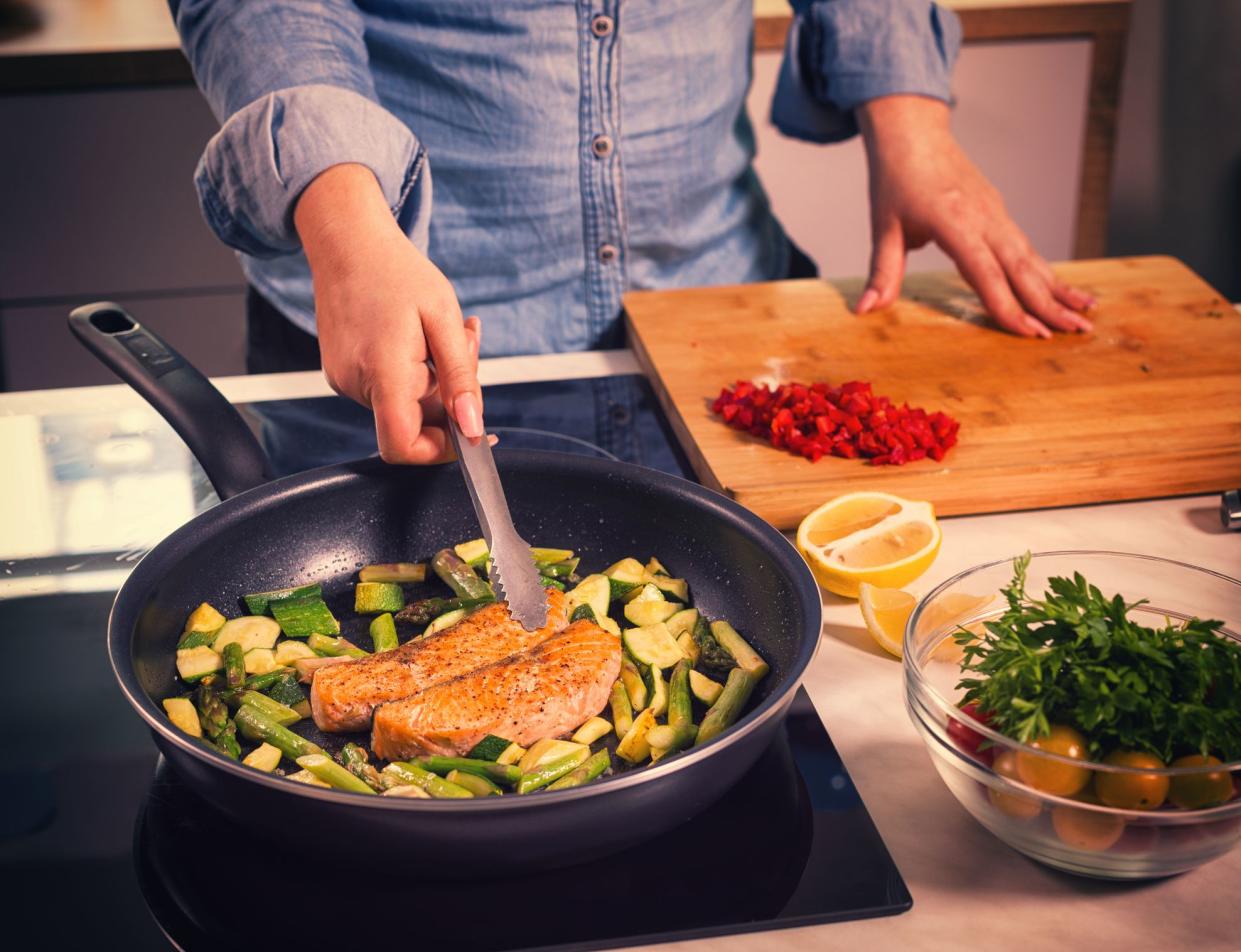 Young women preparing salmon with asparagus and zucchini at home