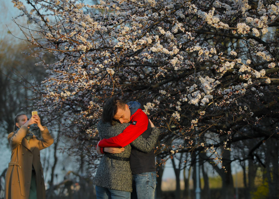 A couple hugs as a girl takes photographs near a blooming tree in Kiev, Ukraine, Wednesday, April 17, 2019. The second round of presidential vote in Ukraine will take place on April 21. (AP Photo/Vadim Ghirda)