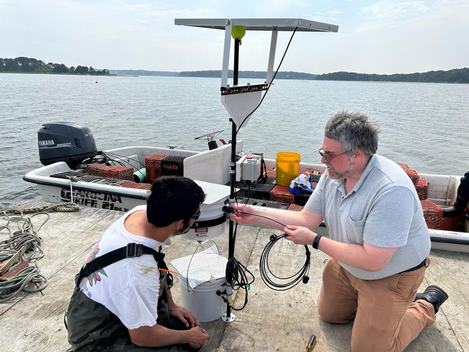 Dave Brown, at right, URI research associate, works on a laser "scarecrow" device with an oyster grower on a platform in Barnstable, Massachusetts.