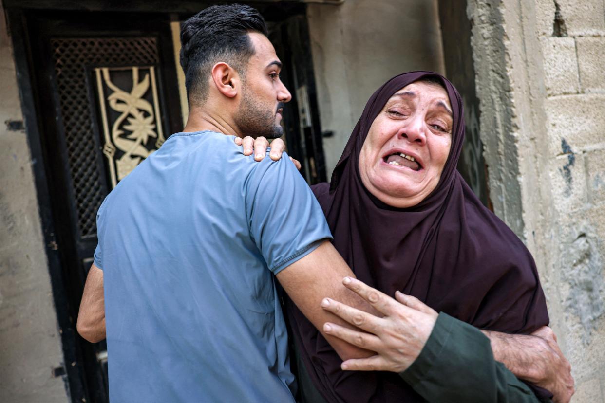 A crying Palestinian woman is consoled by a man as she mourns the loss of loved ones in the aftermath of an Israeli air strike in Rafah in the southern Gaza Strip on October 13, 2023. She is crying at the camera, he is wearing a blue T-shirt, with his back turned.