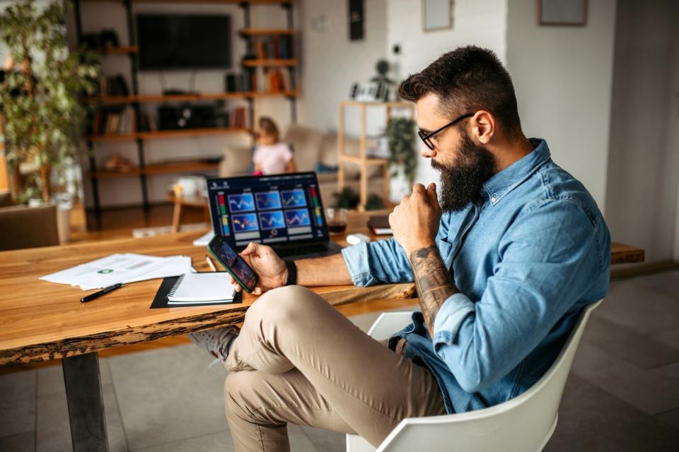 A person looks at their phone in front of a computer screen.