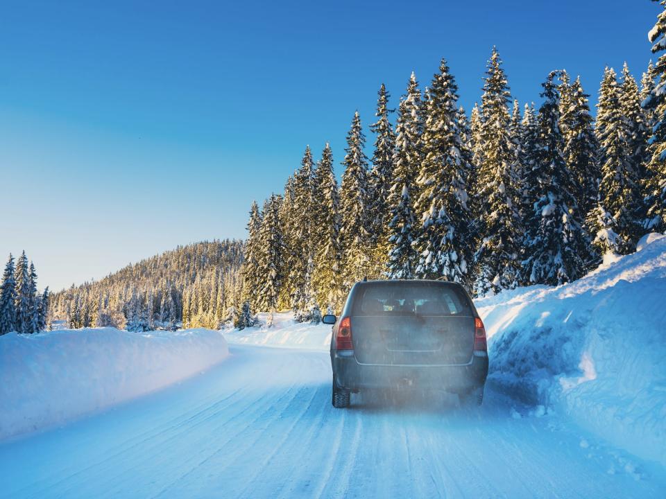 Car getting stuck in snow on road with trees around it