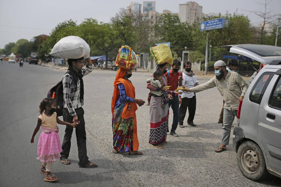 In this Wednesday, May 13, 2020, photo, a family of migrant workers receive bananas and biscuits from a man as they walk along a highway hoping to reach their home, hundreds of miles away, during a nationwide lockdown to curb the spread of new coronavirus in New Delhi, India. Tens of thousands of impoverished migrant workers are on the move across India, walking on highways and railway tracks or riding trucks, buses and crowded trains in blazing heat amid threat to their lives from the coronavirus pandemic. (AP Photo/Altaf Qadri)