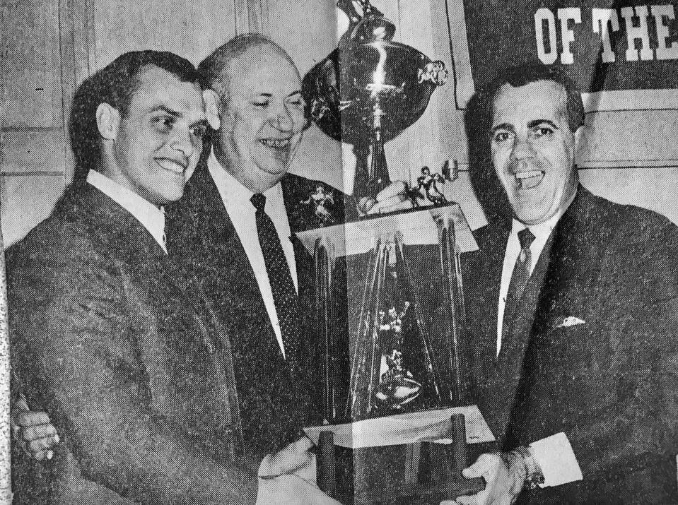 In December 1966, Notre Dame football coach Ara Parseghian, at right, beams as he accepts the 1966 National Championship Trophy from Jerry Liska (center), midwest sports editor for the Associated Press, during a gathering at North Dining Hall at Notre Dame. At left is Robert "Rocky" Bleier, of Appleton, Wis., captain-elect of the team.