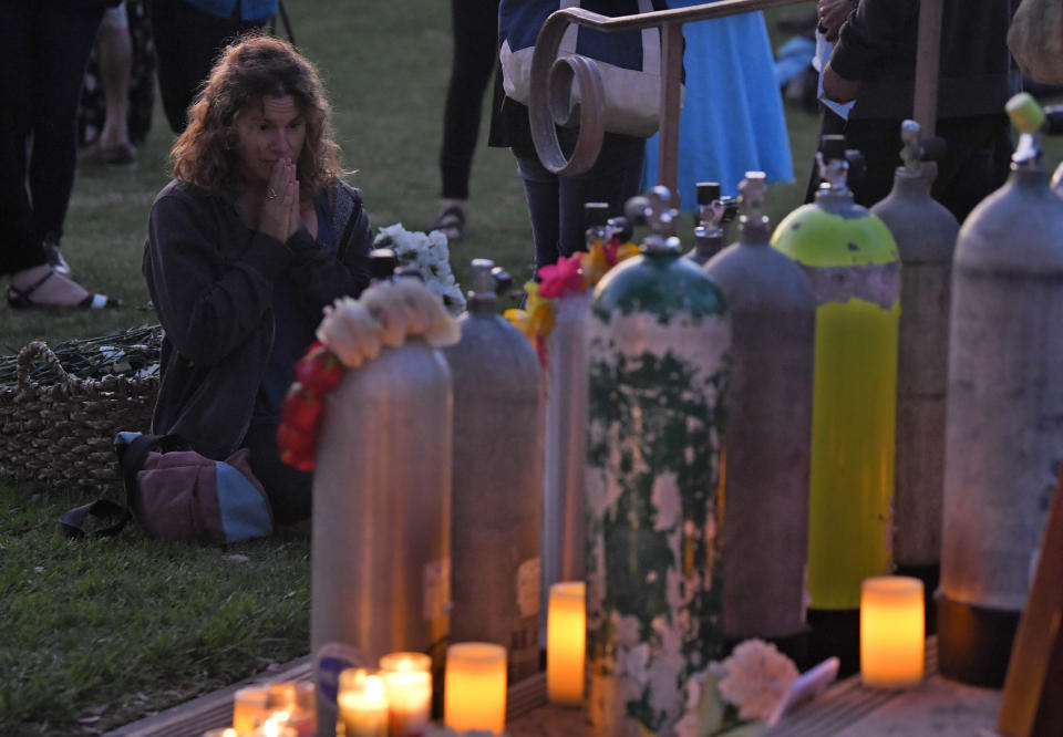 An attendee kneels in front of scuba tanks that were placed to represent each victim during a vigil Friday, Sept. 6, 2019, in Santa Barbara, Calif., for the people who died aboard the dive boat Conception. The Sept. 2 fire took the lives of 34 people on the ship off Santa Cruz Island off the Southern California coast near Santa Barbara. (AP Photo/Mark J. Terrill)