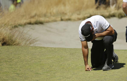Jason Day kneels while waiting to putt on the ninth hole. (AP)