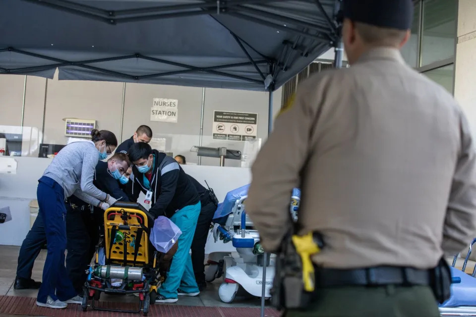A sheriff's deputy watching as health workers attend to a person in a stretcher