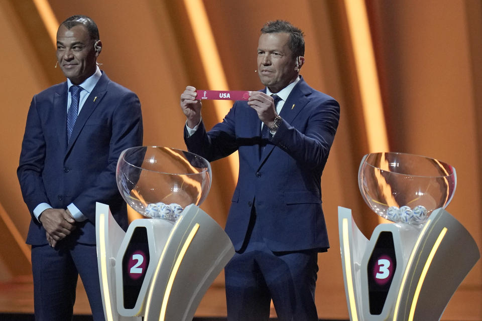 Former Brazilian soccer international Cafu, left, looks on as Former German soccer international and manager Lothar Matthaus holds up the name of the United States as he assists in the 2022 soccer World Cup draw at the Doha Exhibition and Convention Center in Doha, Qatar, Friday, April 1, 2022. (AP Photo/Darko Bandic)