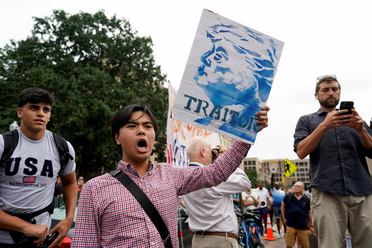 A demonstrator, shouting at the top of his voice, holds up a block-printed placard showing Trump in profile and marked: Traitor.