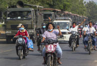 Demonstrators on motor bikes flash the three-fingered salute against the military coup as they ride pass military vehicles parked along a road in Mandalay, Myanmar on Wednesday, Feb. 17, 2021. The U.N. expert on human rights in Myanmar warned of the prospect for major violence as demonstrators gather again Wednesday to protest the military's seizure of power. (AP Photo)