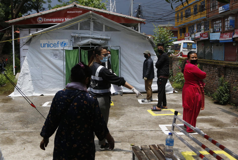 Punam Karmacharya, of the RNA-16 volunteer group, asks people to maintain social distance while waiting for their turn to give swab samples at a hospital in Bhaktapur, Nepal, Tuesday, May 26, 2020. RNA-16 stands for “Rescue and Awareness” and the 16 kinds of disasters they have prepared to deal with, from Nepal’s devastating 2015 earthquake to road accidents. But the unique services of this group of three men and a woman in signature blue vests in the epidemic amount to a much greater sacrifice, said doctors, hospital officials and civic leaders. (AP Photo/Niranjan Shrestha)