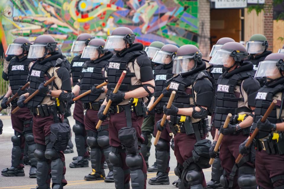 Armored members of the Minneapolis State Patrol stand guard in an intersection in front of burned out buildings in the Third Precinct of Minneapolis on Friday. The area was rocked by looting and widespread destruction overnight by protesters and rioters following peaceful gatherings for most of the day. Protesters were demanding justice for the death of George Floyd, who died after a white police officer knelt on his neck. Friday, May 29, 2020