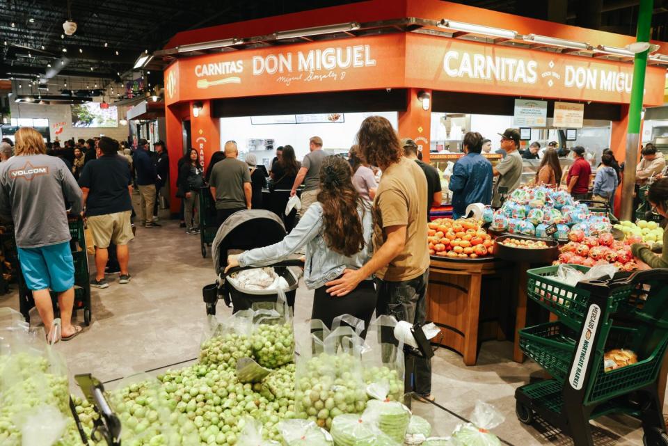 Shoppers milling around the produce section of a grocery store.