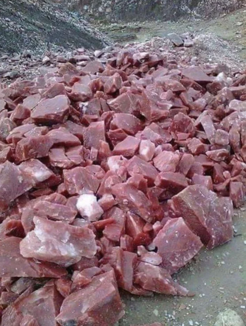A large pile of uncut, raw red rocks scattered on the ground in a quarry