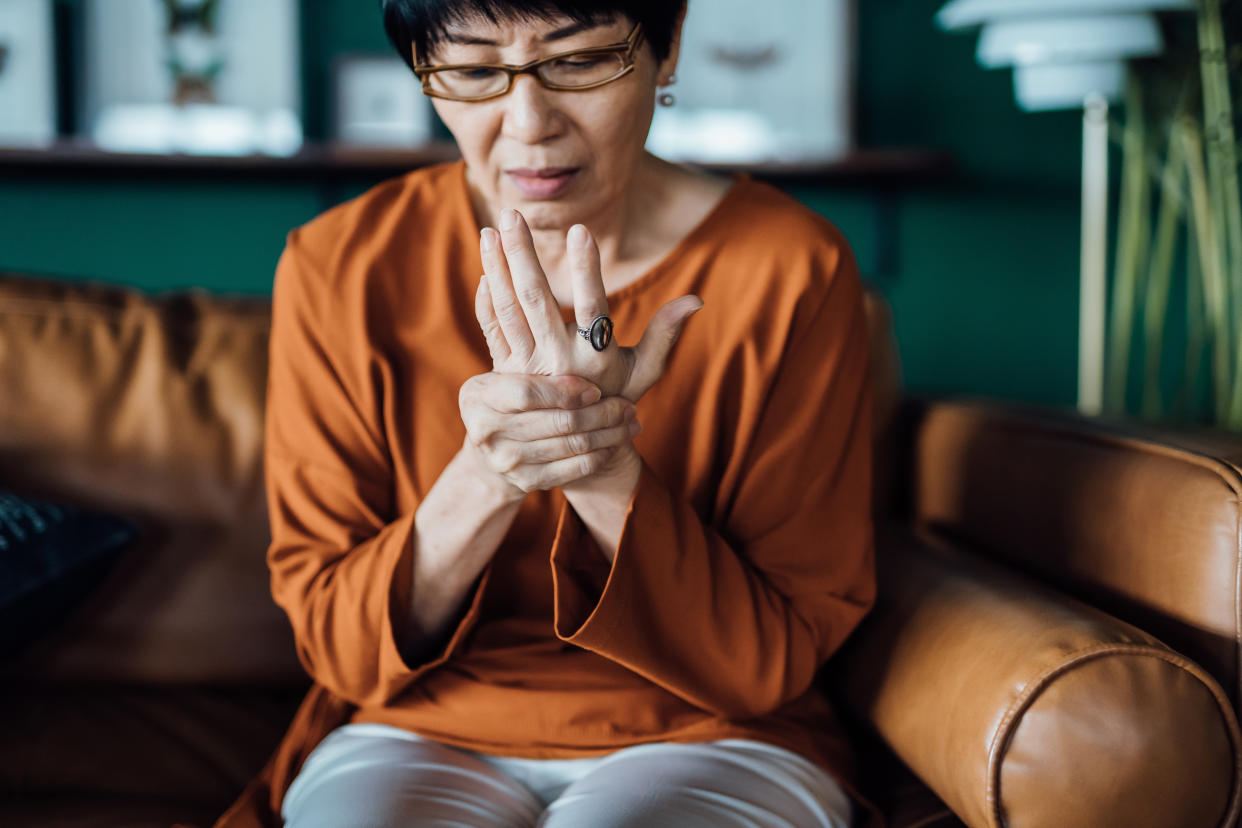 Photo of a woman with health issues, rubbing her hands in discomfort.