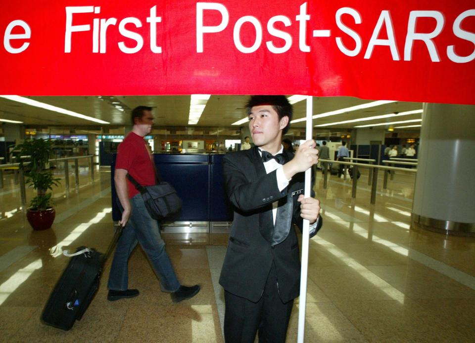 A Chinese man holds up a banner welcoming the first foreign tour group to arrive at the Beijing airport after the SARS epidemic in Beijing, Monday, June 30, 2003.