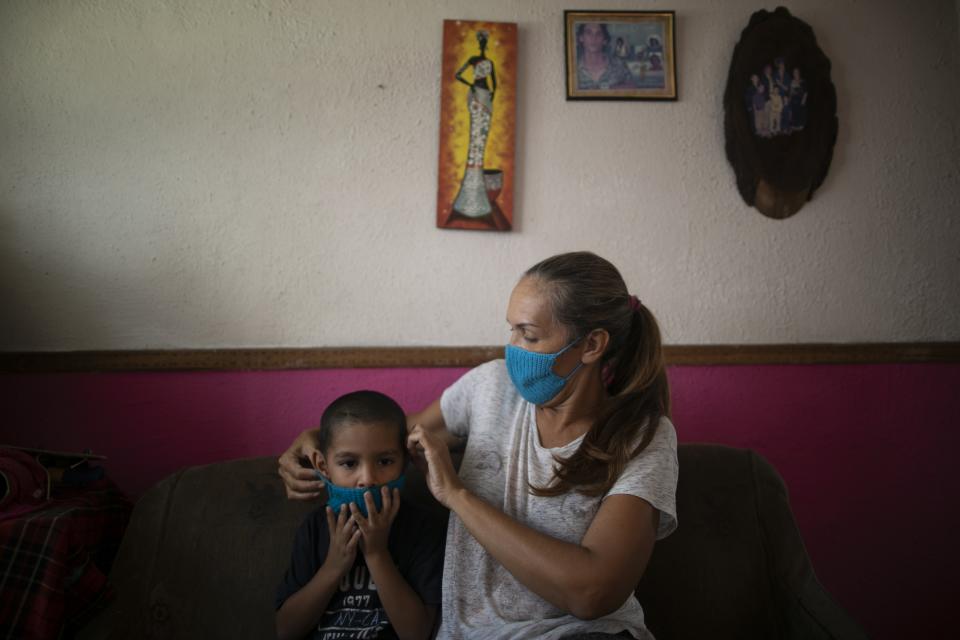 In this April 24, 2020 photo, Maylin Perez who says the potential spread of the new coronavirus virus weighs on her heavily, puts a knitted face mask on her grandson Daniel Cocho, in their apartment in Caracas, Venezuela. Perez knits the colorful face masks to barter for extras besides the lentils and rice she receives from a monthly, government subsidized box of food. (AP Photo/Ariana Cubillos)