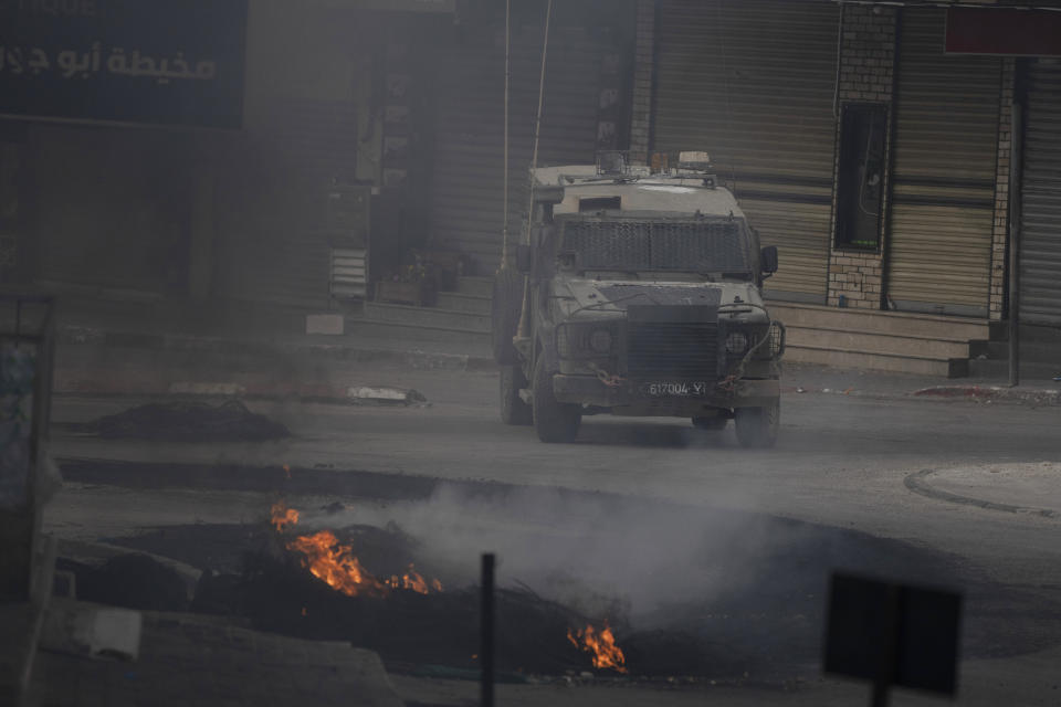 An Israeli armoured vehicle moves near burning tires during clashes with Palestinian demonstrators in the West Bank city of Jenin, Wednesday, May 22, 2024. (AP Photo/Leo Correa)