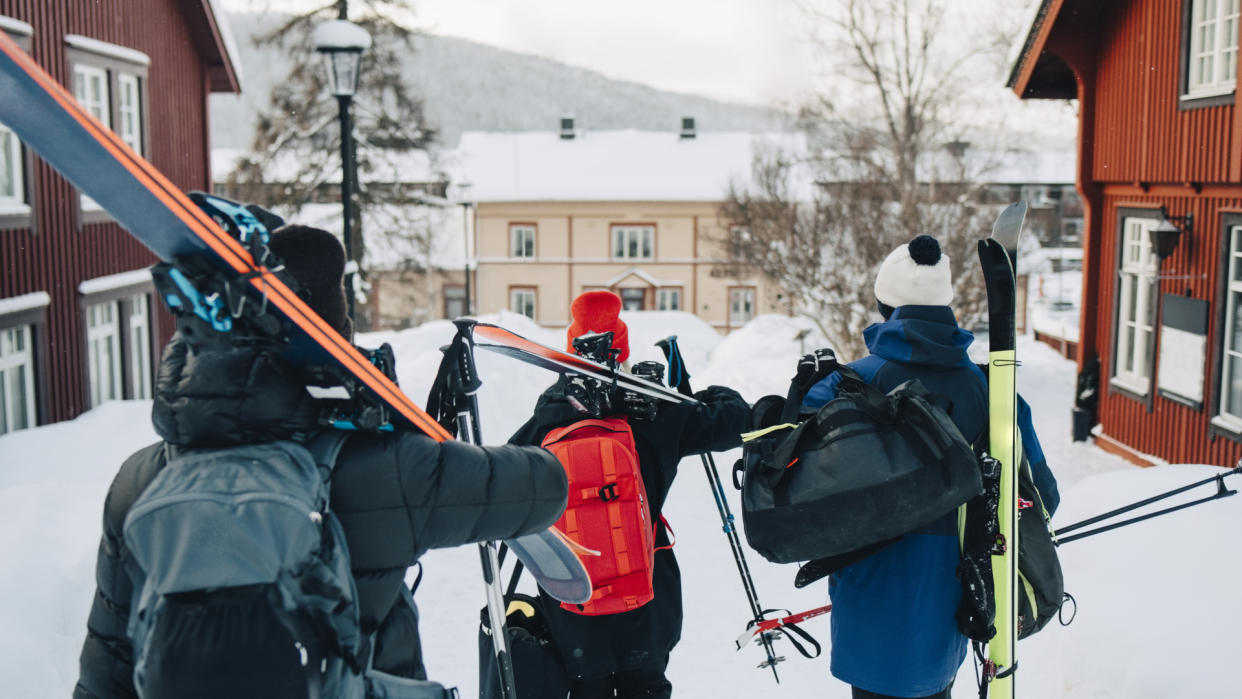  Three skiers walking through a resort with skis over their shoulders. 