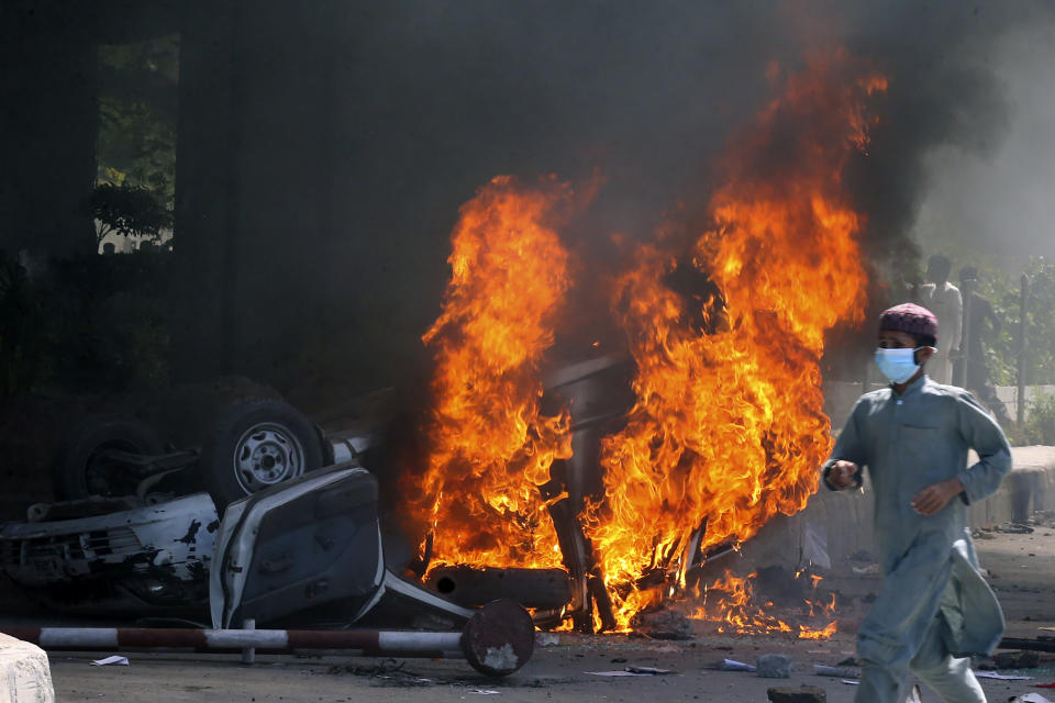 A man runs past a burning car set on fire by angry supporters of Pakistan's former Prime Minister Imran Khan during a protest against the arrest of their leader, in Peshawar, Pakistan, Wednesday, May 10, 2023. A court has ruled that former Pakistani Prime Minister Imran Khan can be held for questioning for eight days. The decision Wednesday comes a day after the country’s popular opposition leader was dragged from a courtroom and arrested. His detention set off clashes between his supporters and police Tuesday. (AP Photo/Muhammad Sajjad)