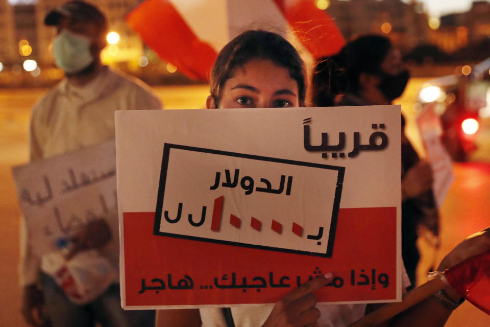 An anti-government protester holds a placard in Arabic that reads "Soon $ 1 = 10000 Lebanese pounds, if you are not happy, immigrate," during a protest against the political leadership they blame for the economic and financial crisis, in front of the government house in downtown Beirut, Lebanon, Thursday, June 11, 2020. (AP Photo / Hussein Malla)