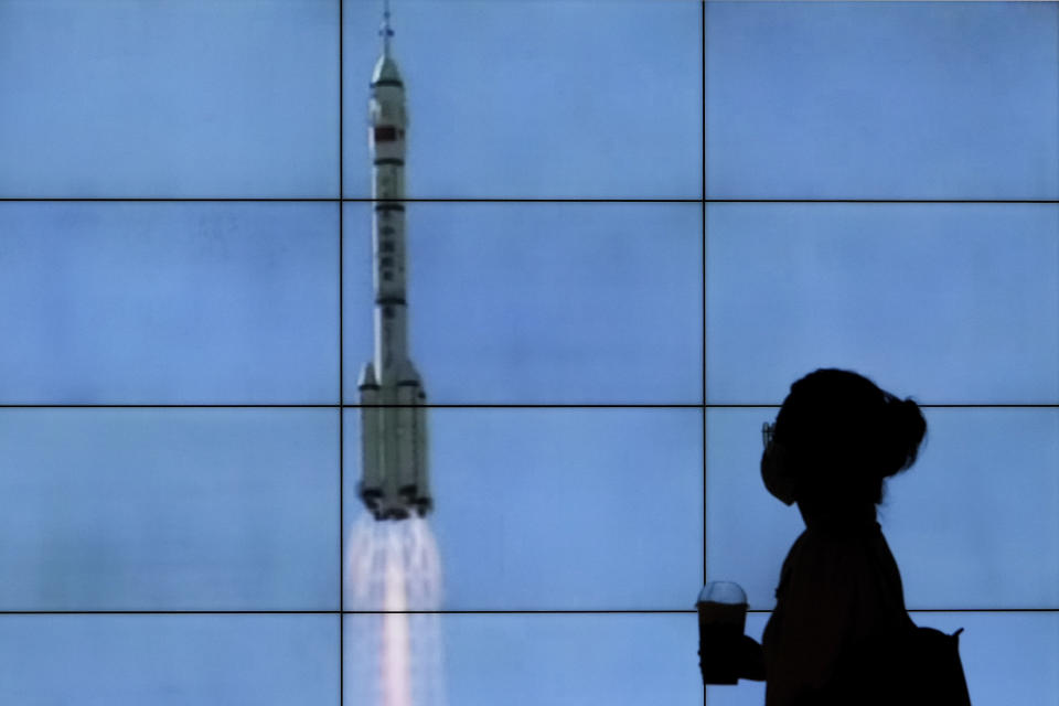 A woman wearing a face mask is silhouetted as she walks by a TV screen showing CCTV live telecast of the Long March-2F Y12 rocket carrying a crew of Chinese astronauts in a Shenzhou-12 spaceship lifts off at the Jiuquan Satellite Launch Center, at a shopping mall in Beijing, Thursday, June 17, 2021. China launched the first three crew members on a mission to its new space station Thursday in its first crewed mission in five years. (AP Photo/Andy Wong)