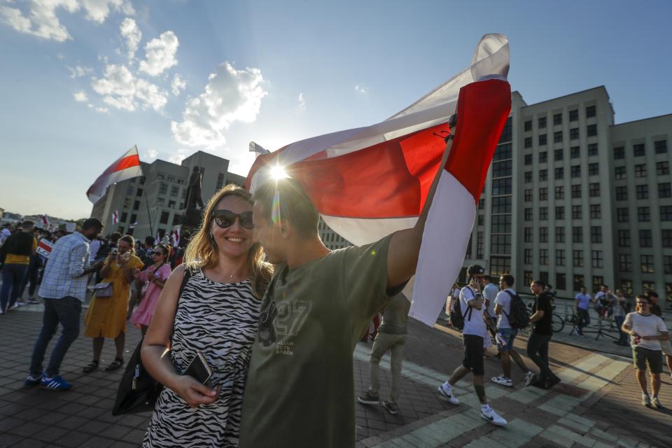 A couple cover themselves with an old Belarusian national flag, enjoy a sunset during opposition rally in front of the government building in Minsk, Belarus, Monday, Aug. 17, 2020. Workers heckled President Alexander Lukashenko as he visited a factory and strikes grew across Belarus, raising the pressure on the authoritarian leader to step down after 26 years in power. (AP Photo/Sergei Grits)