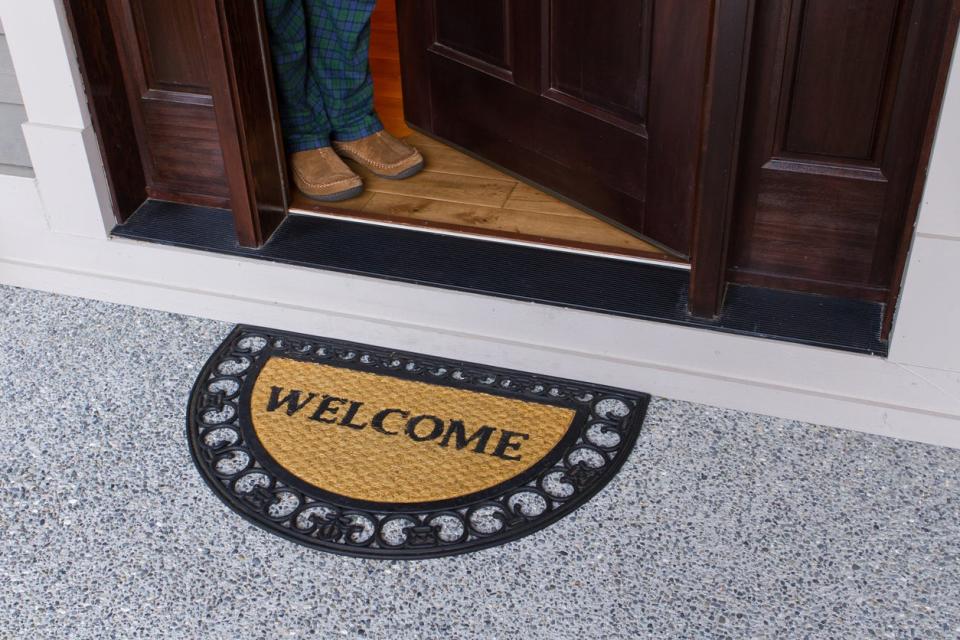 Welcome door mat on a porch and open door, person's legs visible inside the door.