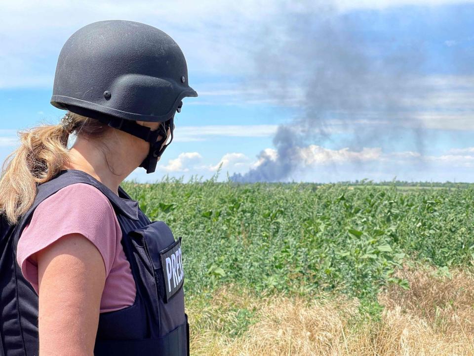 Nadja Kriewald mit Schutzhelm im Kriegsreporter-Einsatz in der Ukraine. Ihr Blick richtet sich auf ein Feld, an dessen Horizont offenbar etwas brennt. (Bild: Francisco De La Torre)