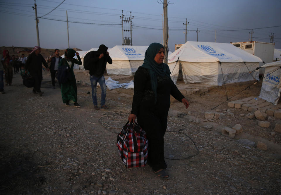 Syrians who are newly displaced by the Turkish military operation in northeastern Syria, carry their belongings as they walk to receive their tents, at the Bardarash camp, north of Mosul, Iraq, Wednesday, Oct. 16, 2019. The camp used to host Iraqis displaced from Mosul during the fight against the Islamic State group and was closed two years ago. The U.N. says more around 160,000 Syrians have been displaced since the Turkish operation started last week, most of them internally in Syria. (AP Photo/Hussein Malla)