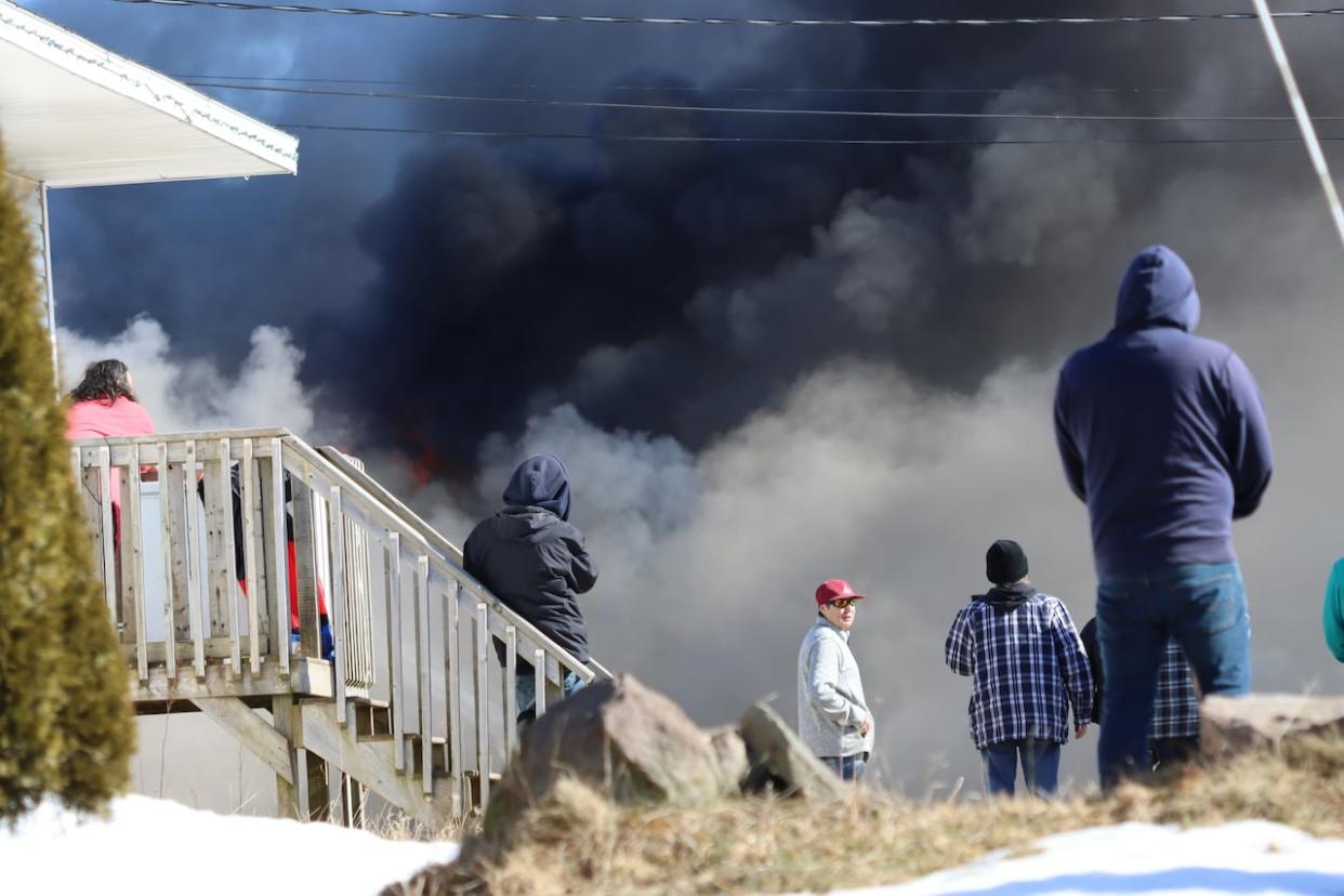 Neighbours watch as smoke billows from a house fire caused by an RCMP stun grenade during an arrest in Eskasoni First Nation in February 2023. (Erin Pottie/CBC - image credit)