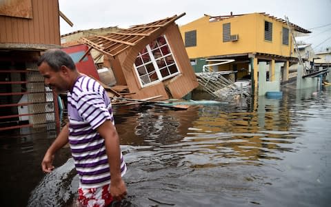 A man walks past destroyed homes in Catano, Puerto Rico, which was pummelled by Hurricane Maria in 2017 - Credit: AFP