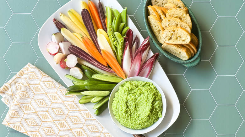 Herby spring pea dip on platter with crudites and toasted baguette slices