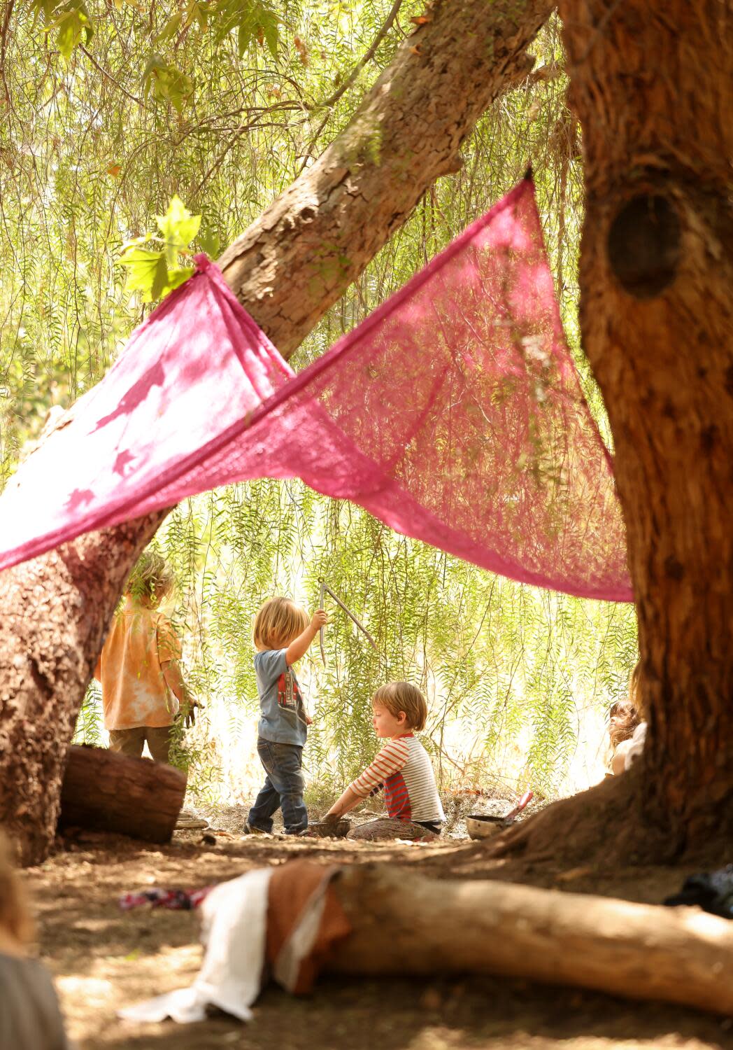 Children play under a shade cloth strung between trees.