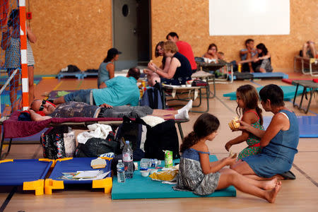 Tourists, who were evacuated due to a forest fire, rest on mats and cots and eat a meal in a gymnasium in Bormes-les-Mimosas, in the Var department, France, July 26, 2017. REUTERS/Jean-Paul Pelissier