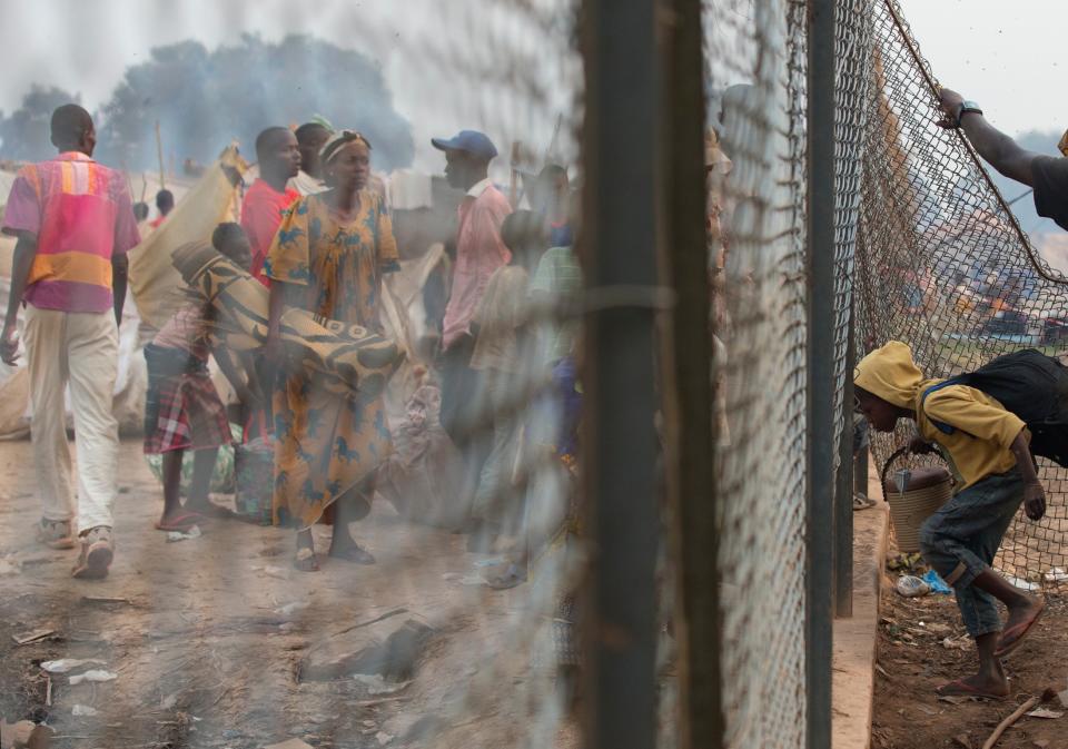 A section of fence is held open for a girl to climb through, as families who had been sleeping in a food distribution area are moved out with the help of French troops, in an informal camp housing an estimated 100,000 displaced people, at Mpoko Airport in Bangui, Central African Republic, Wednesday, Jan. 8, 2014. Food and supplies distribution by the World Food Program and the United Nations Refugee Agency began Tuesday and was expected to last 10 days. It is the first aid delivery to reach the camp since Dec. 15, and many families were lacking food or even rudimentary shelter from the harsh daytime sun and chilly nights. Residents were receiving supplies including rice, cooking oil, tarps, mats, and blankets. (AP Photo/Rebecca Blackwell)