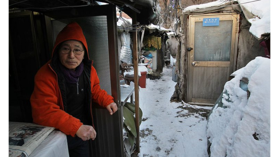 Un hombre mayor surcoreano sentado en el barrio humilde de Guryong de Seúl con nieve en el suelo.