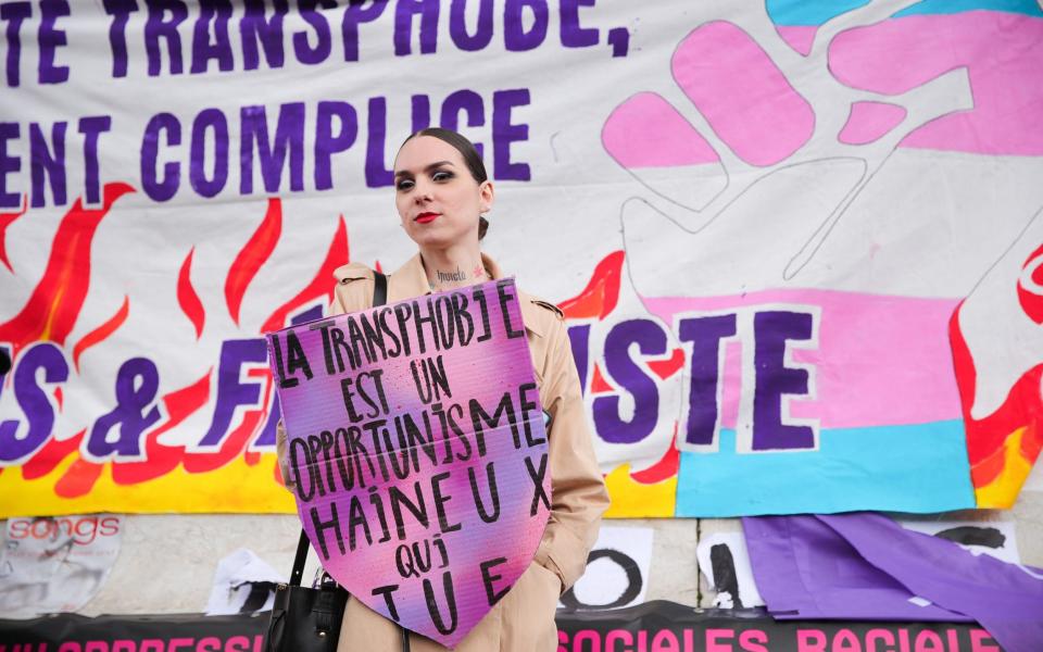 A woman in France holds a banner saying  'Transphobia is hateful opportunism that kills'