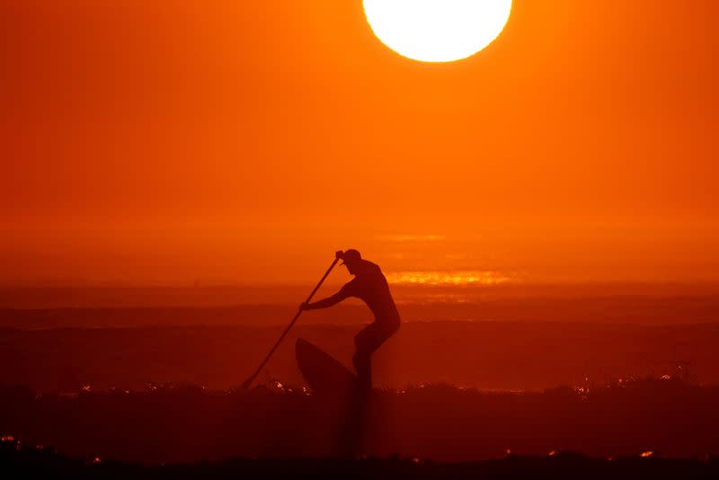 FILE PHOTO: A man on a paddle board surfs as a heat wave hits France