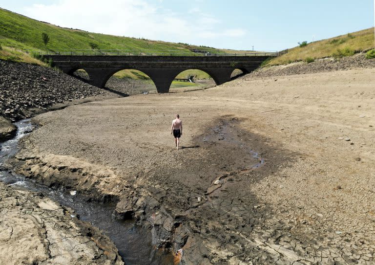 Una persona camina por una orilla seca de un afluente del embalse de Dowry, cerca de Oldham, Inglaterra, el lunes 18 de julio de 2022, mientras continúa la ola de calor en el Reino Unido. 