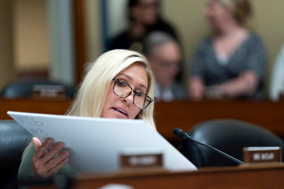 Rep. Marjorie Taylor-Greene  wearing glasses looking at a big piece of cardboard, with only the back visible to the camera