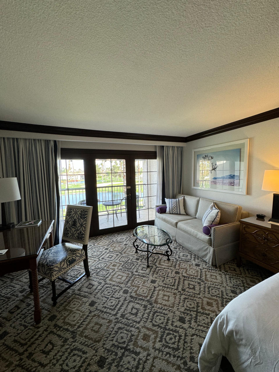 Hotel room interior with a sofa, armchair, and bed, leading to a balcony